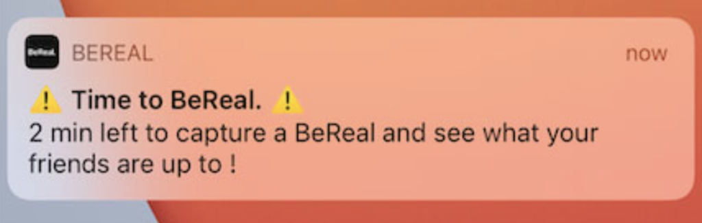 The BeReal notification: An iOS notificaiton bubble with the words "Time to be real" surrounded by two warning symbols. Below the  warning is the words "2 min left to capture a BeReal and see what your friends are up to !"